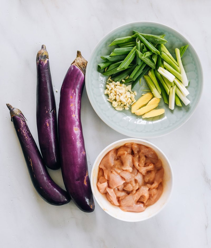 Whole eggplant, chicken, and aromatics on white marble