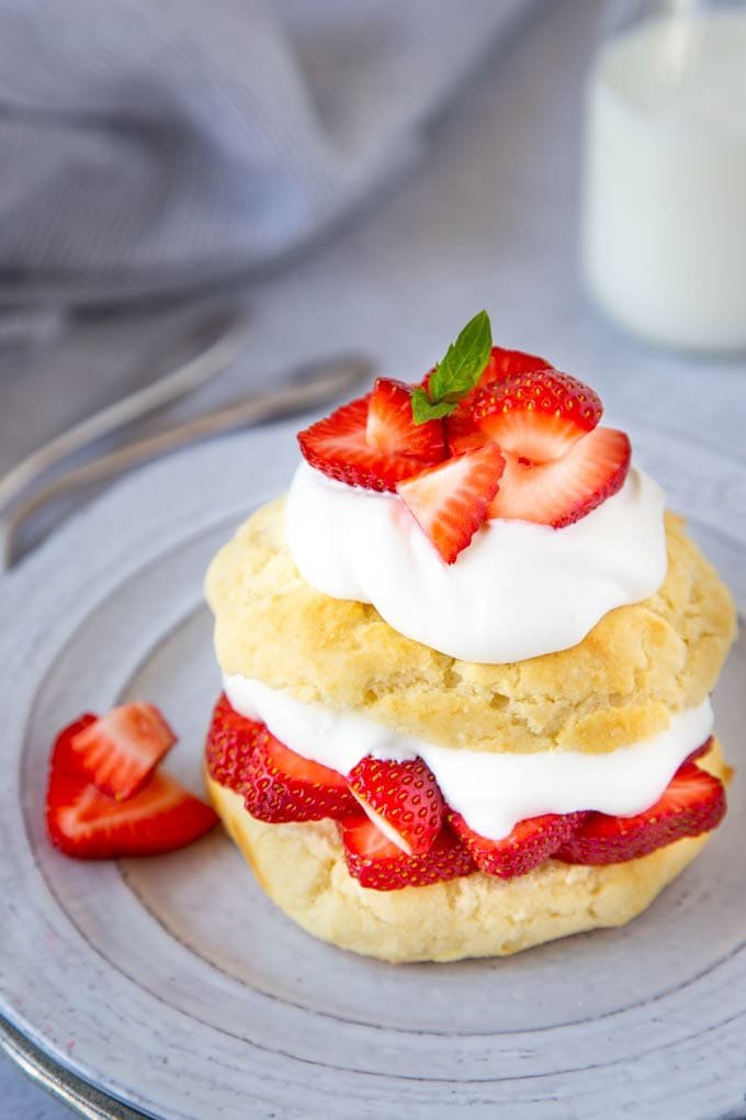 Sliced strawberries with whipped cream beside shortcake biscuits