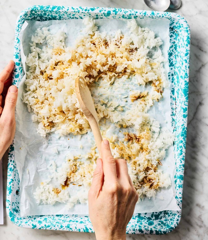 Rice being stirred on a parchment-lined baking tray
