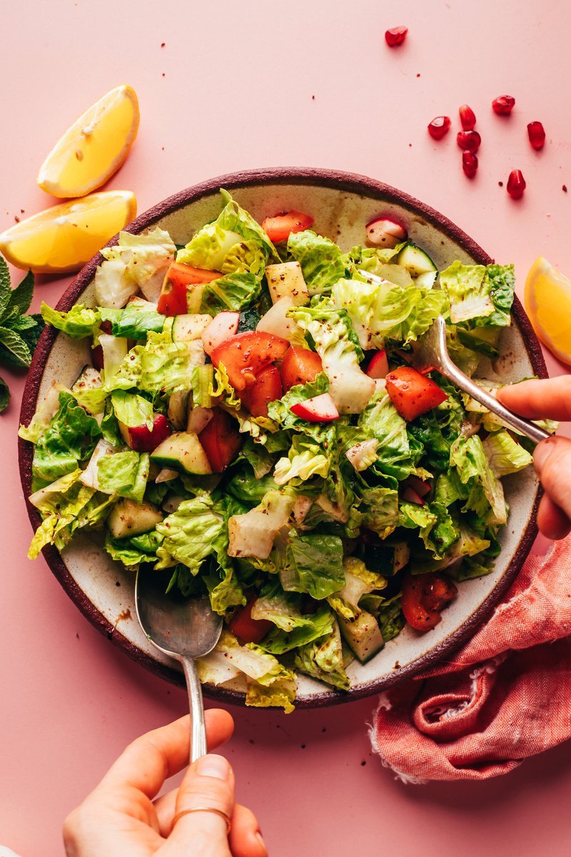 Hands tossing romaine and vegetables with pomegranate dressing