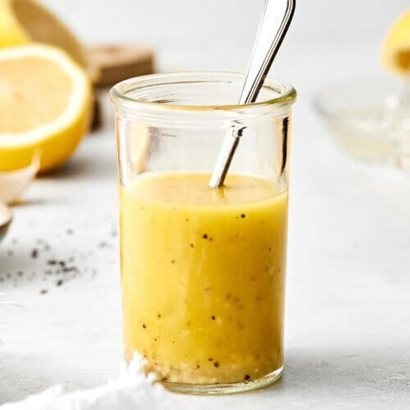 Lemon vinaigrette in a small clear glass bottle with a lemon garnish