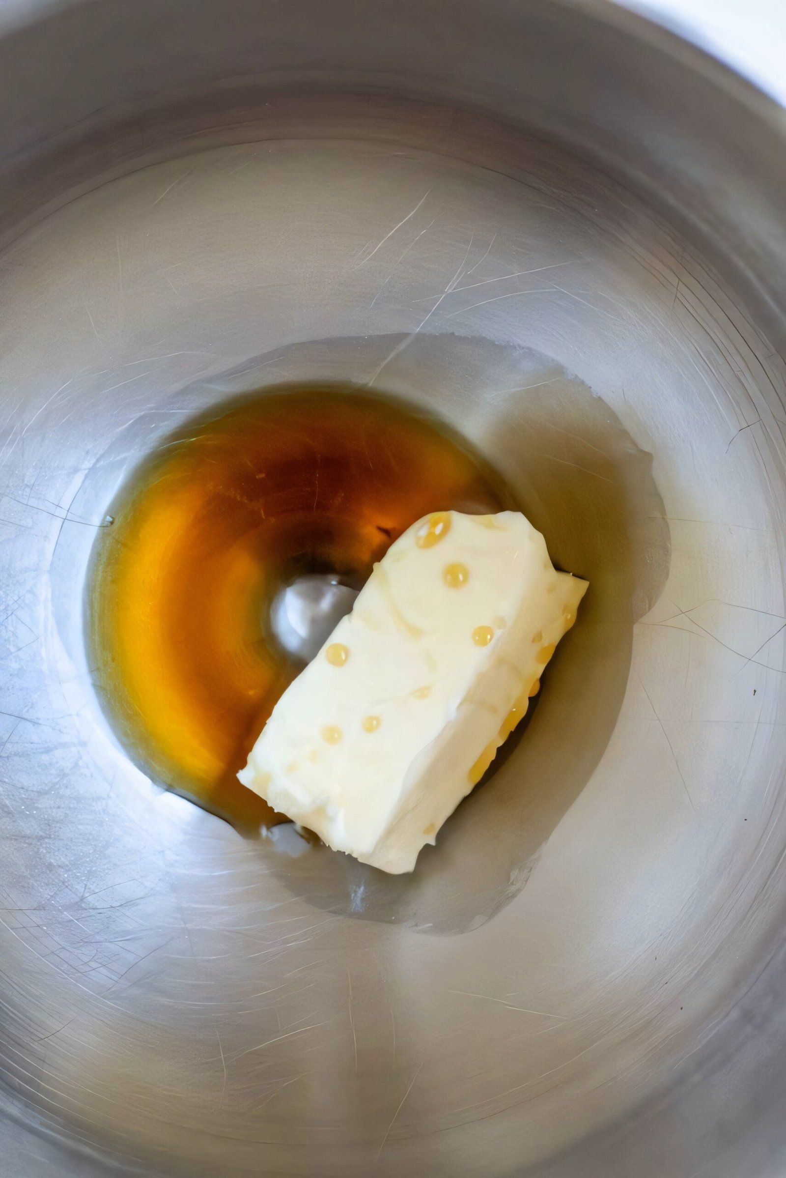 Maple syrup being poured into softened butter in a mixing bowl