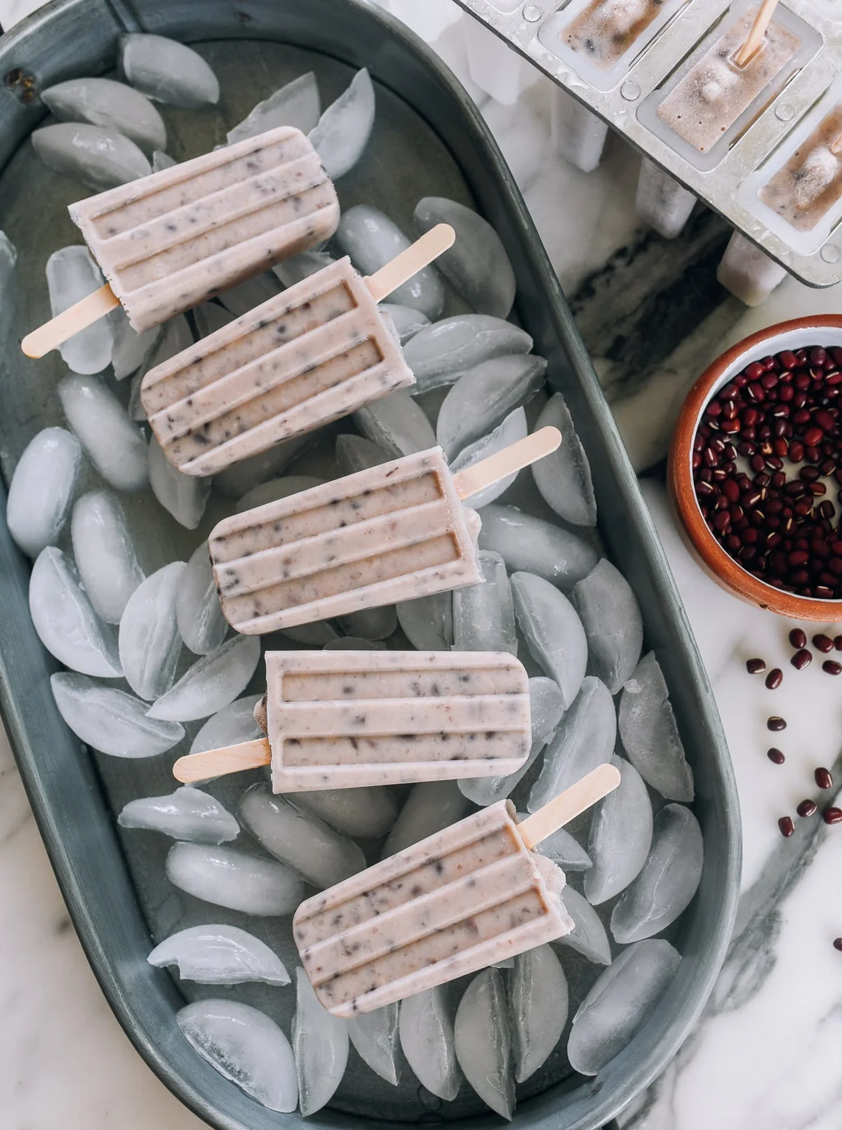 Red bean popsicles on ice in a popsicle mold with adzuki beans