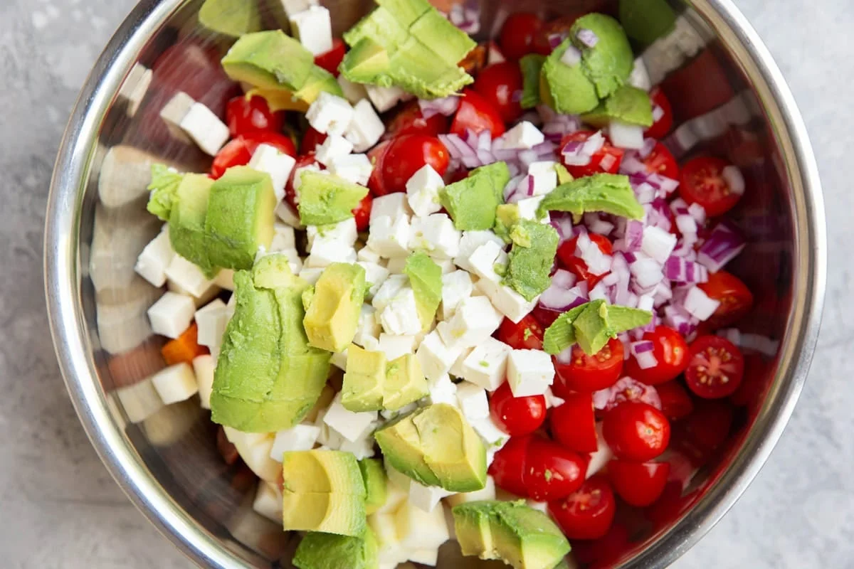 Chopped avocado, feta, cherry tomatoes, and red onion ready in a mixing bowl