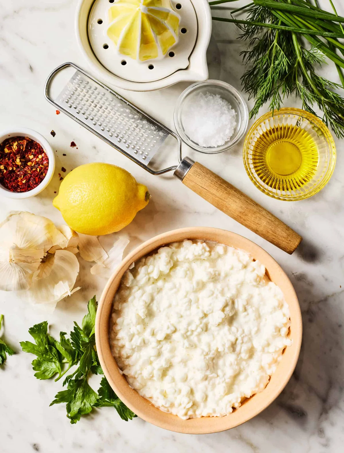 Flat-lay of cottage cheese and ingredients including lemon, garlic, herbs, olive oil, and salt