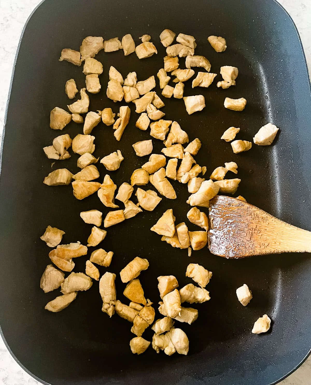 Diced chicken pieces browning in a nonstick skillet