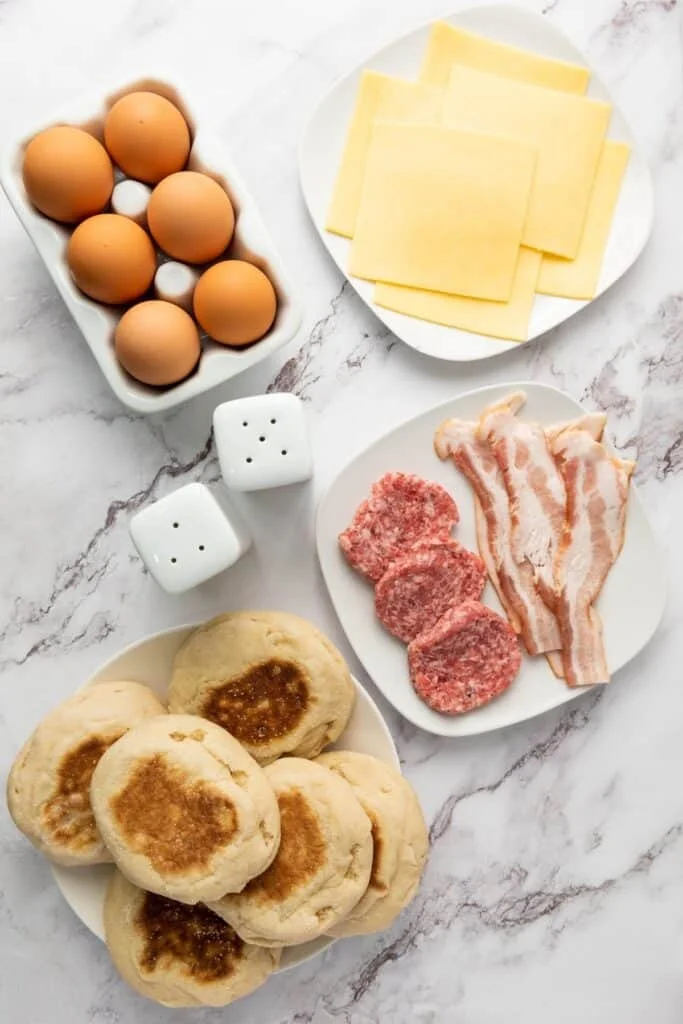 Eggs, cheese, bacon, sausage and muffins laid out for assembly
