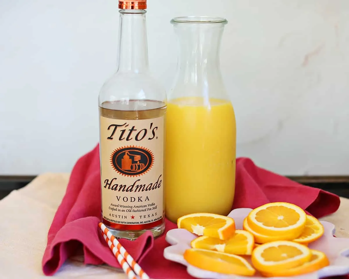 Vodka bottle, carafe of orange juice, and orange slices on a red napkin