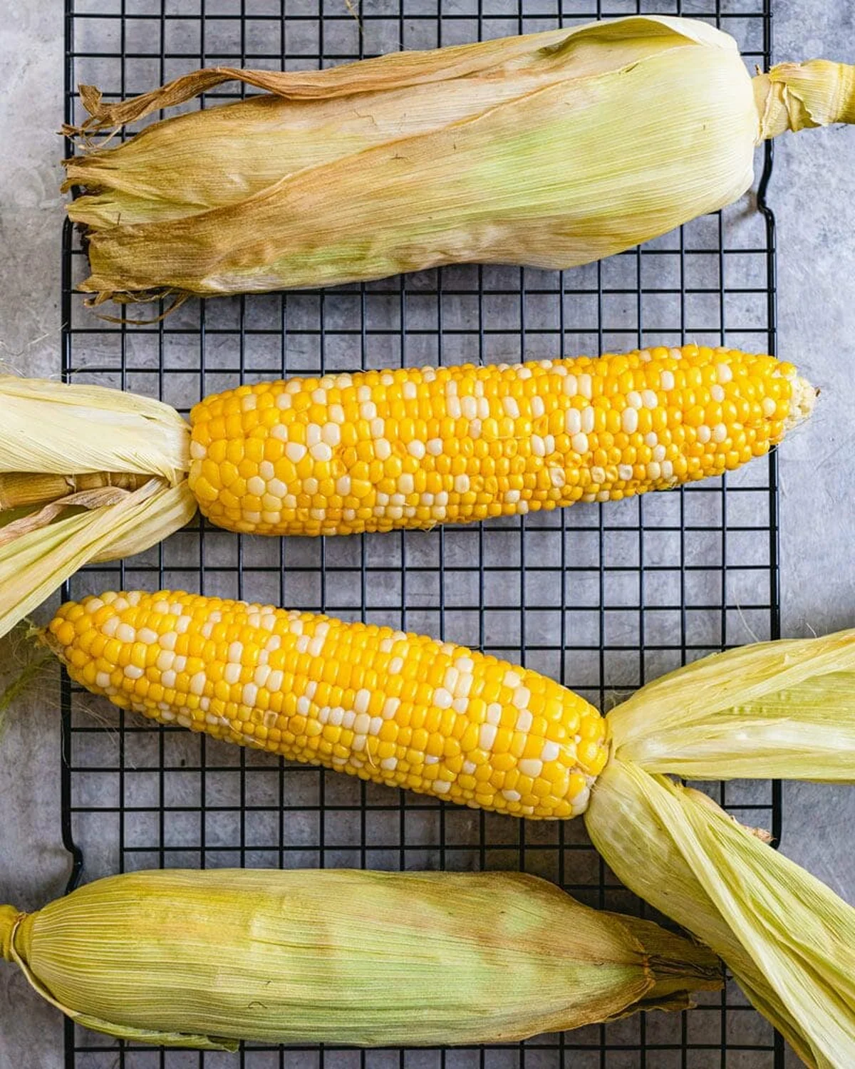 Fresh sweet corn cobs with husks peeled back on a rack