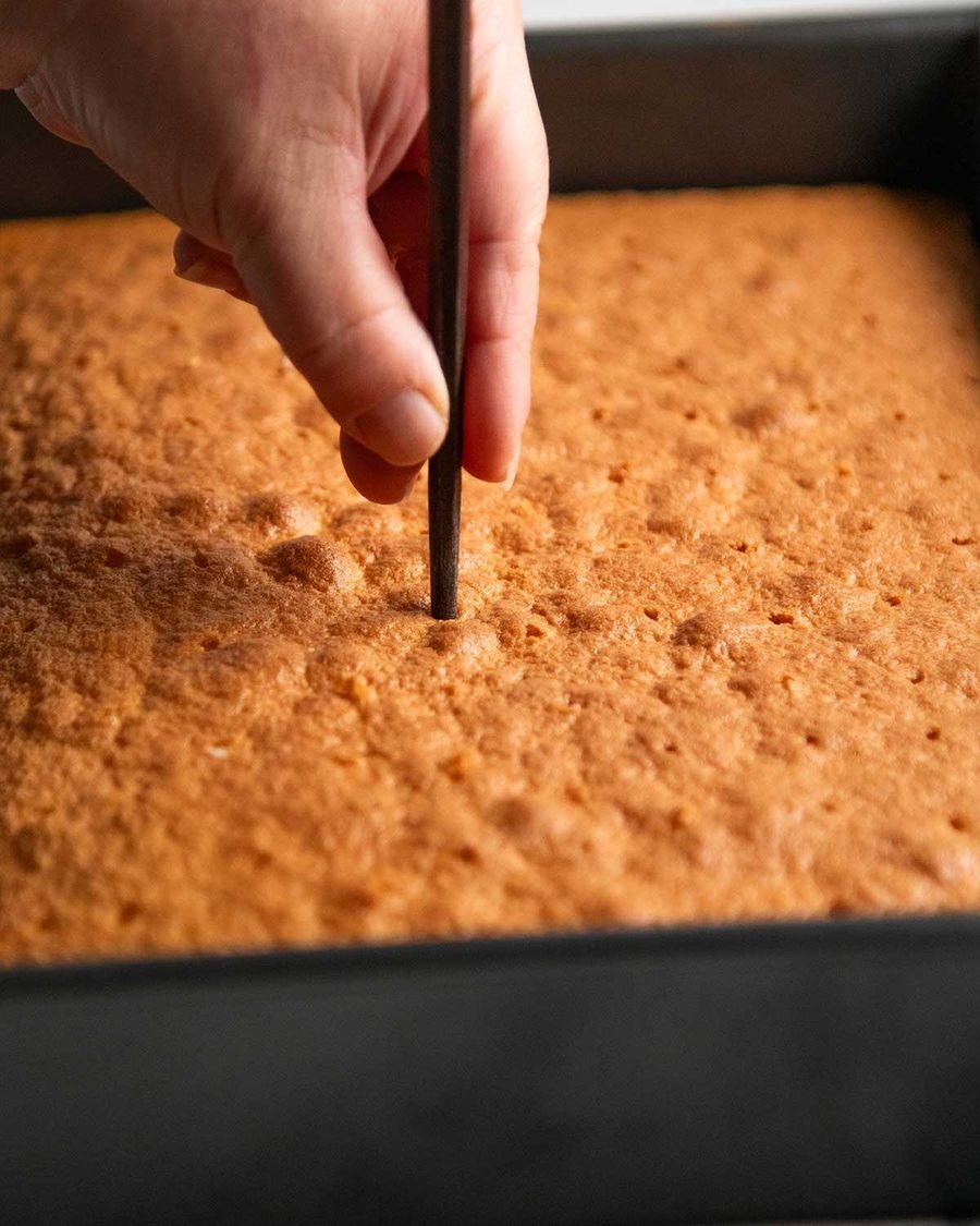 Golden sponge cake in a pan being poked with a chopstick