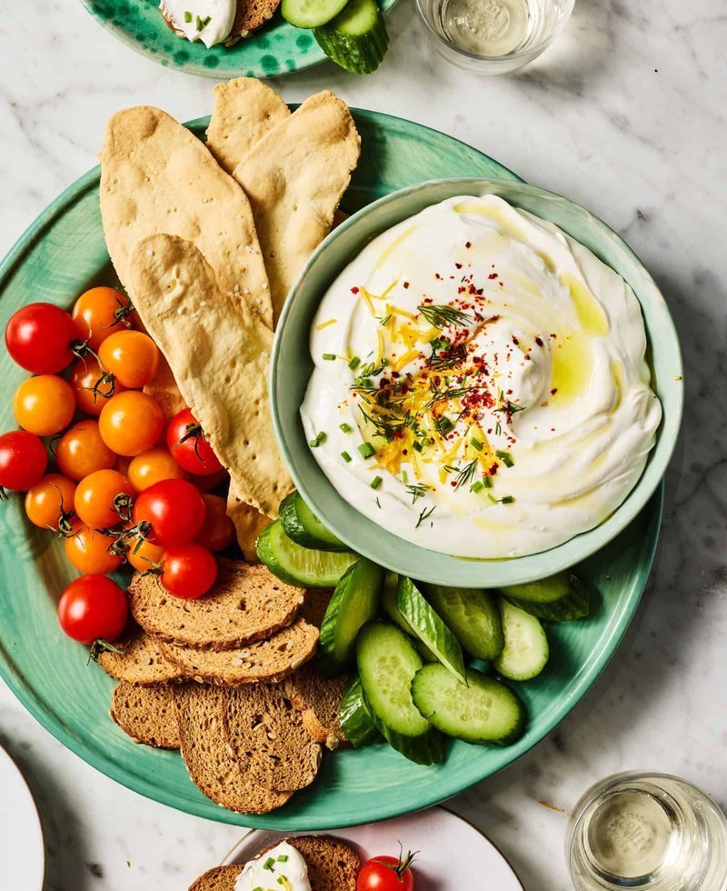Bowl of whipped cottage cheese with pita, bread, cherry tomatoes, and cucumber for dipping