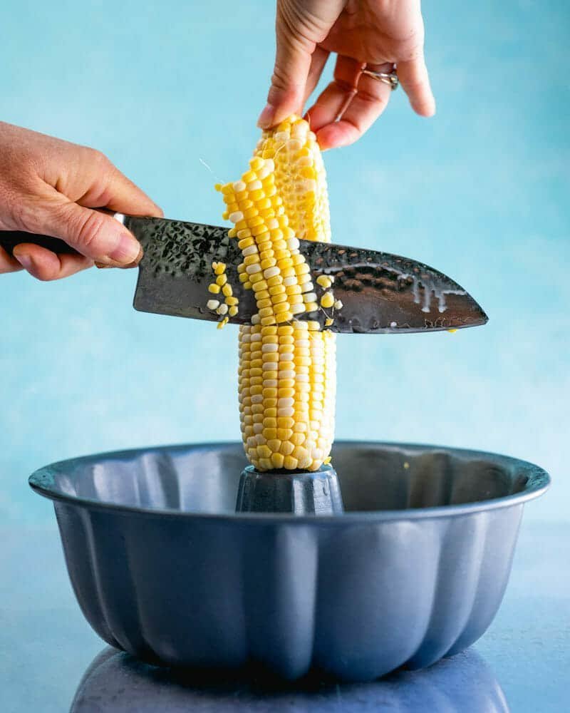 Knife slicing sweet corn kernels off the cob into a bowl