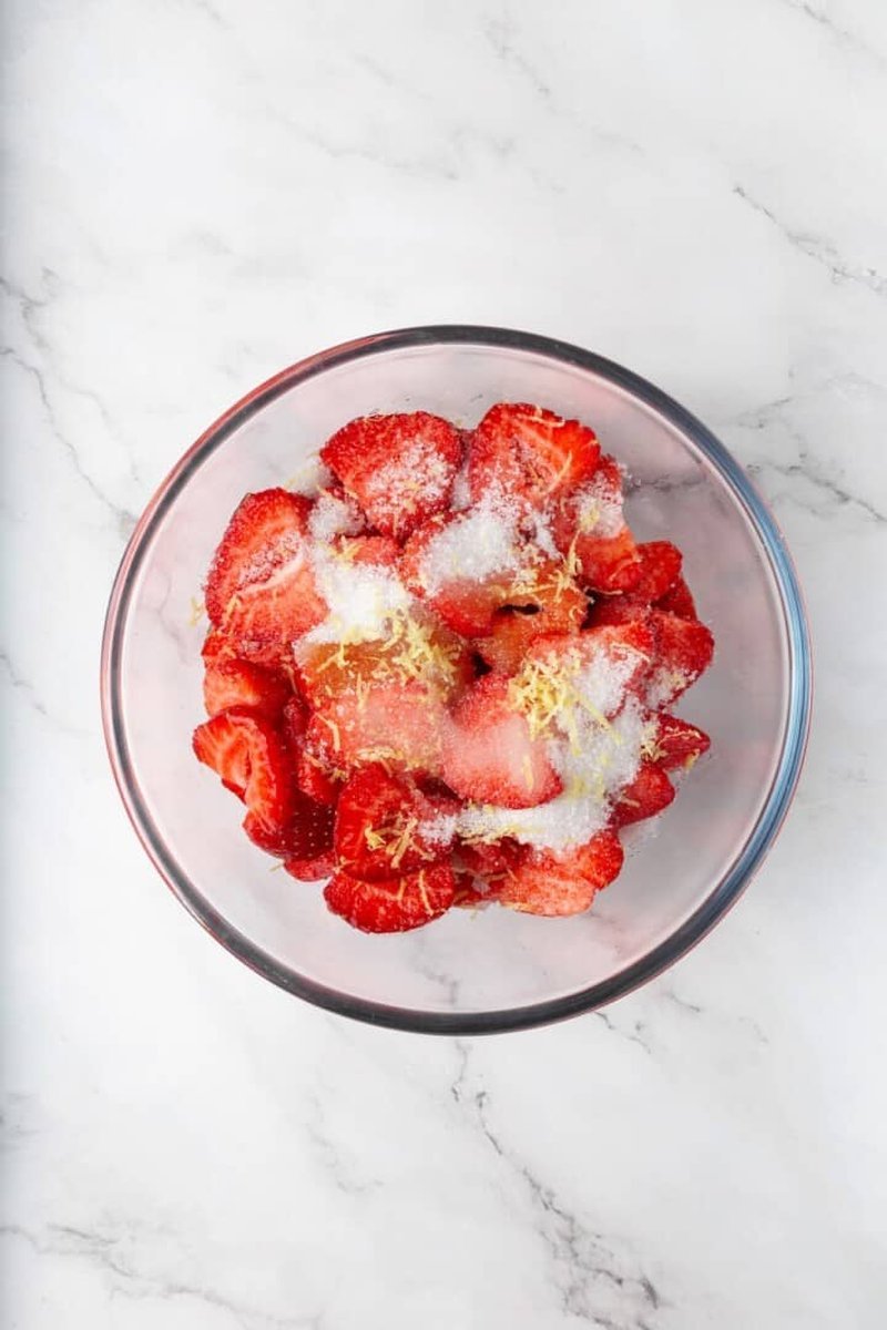 Sliced strawberries being tossed with sugar and lemon zest