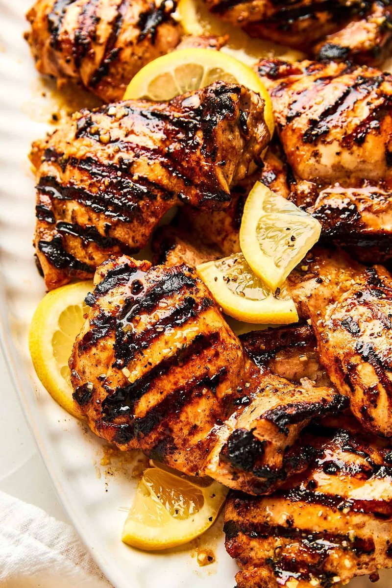 Close-up of glossy grilled chicken thighs with lemon wedges