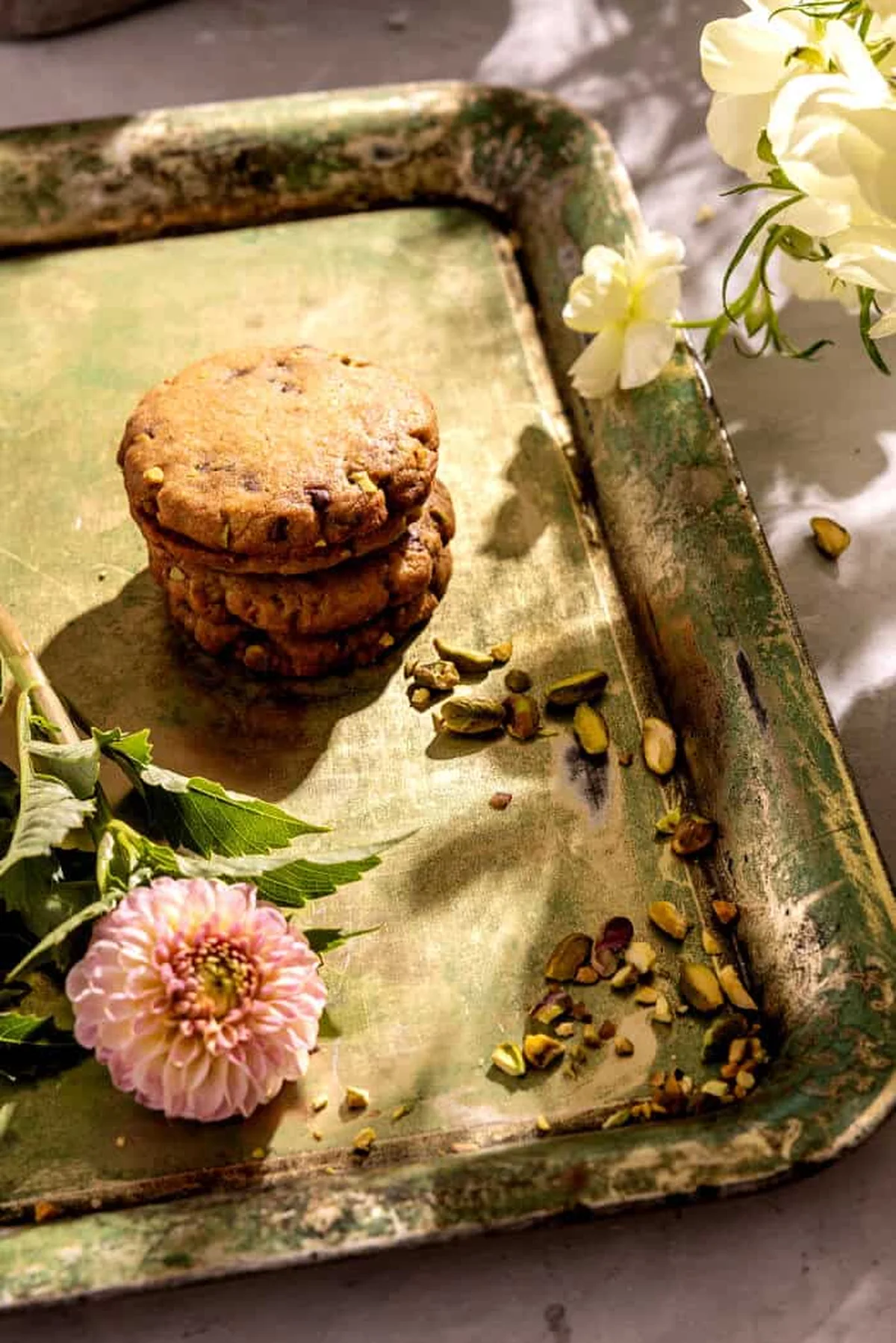 Stack of pistachio chocolate chip cookies beside fresh flowers