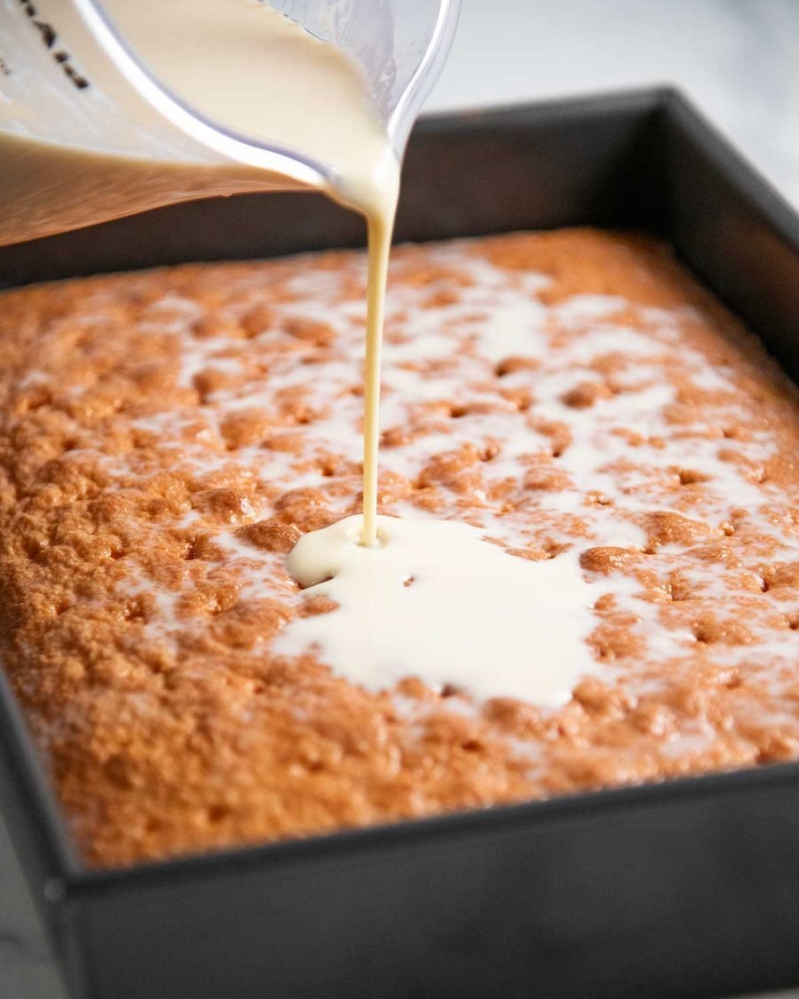 Three-milk mixture being poured over poked sponge cake in pan