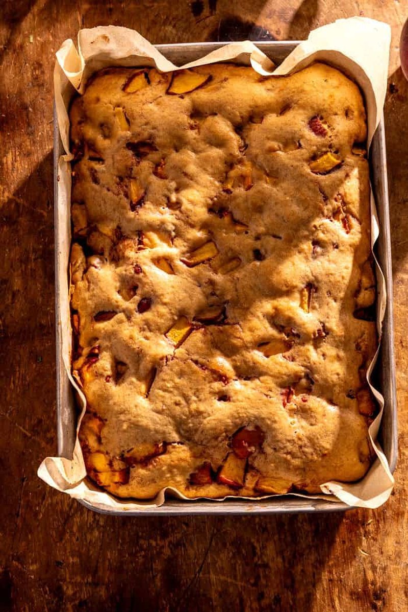 Unbaked cake batter studded with peaches in parchment-lined pan