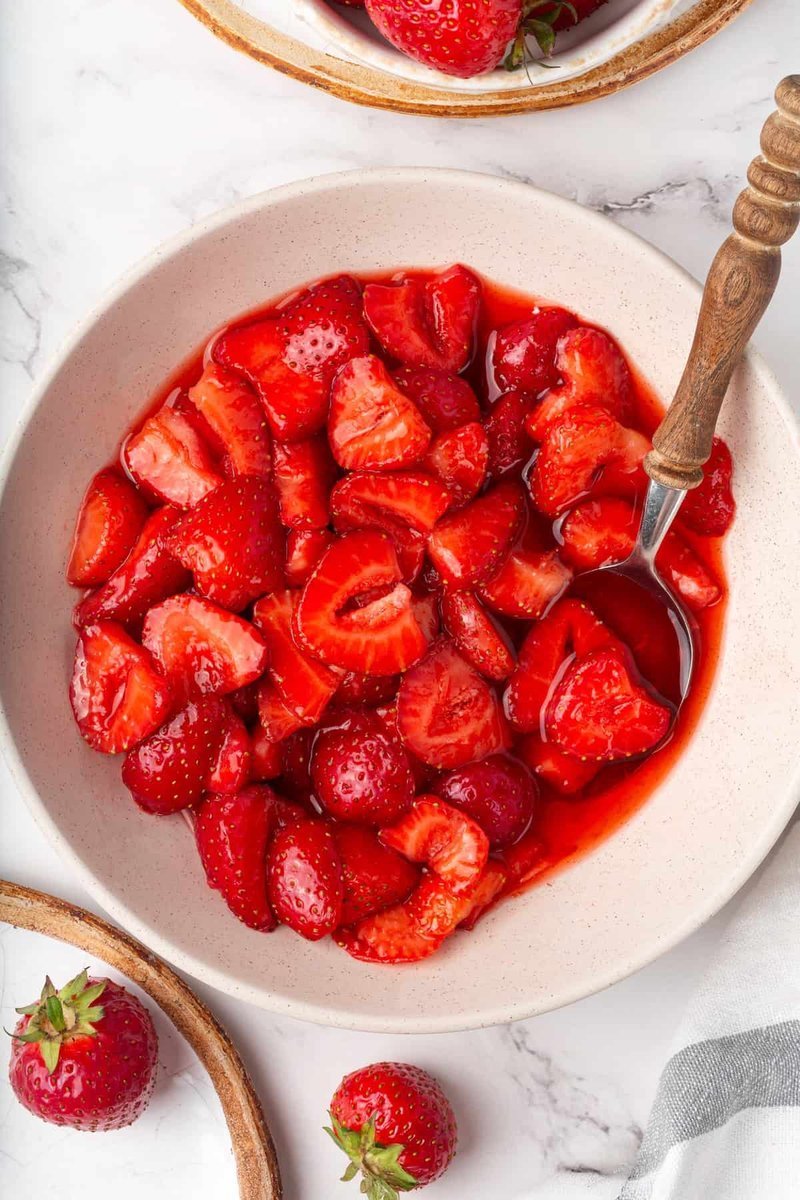 Macerated strawberries in a speckled ceramic bowl with a wooden spoon