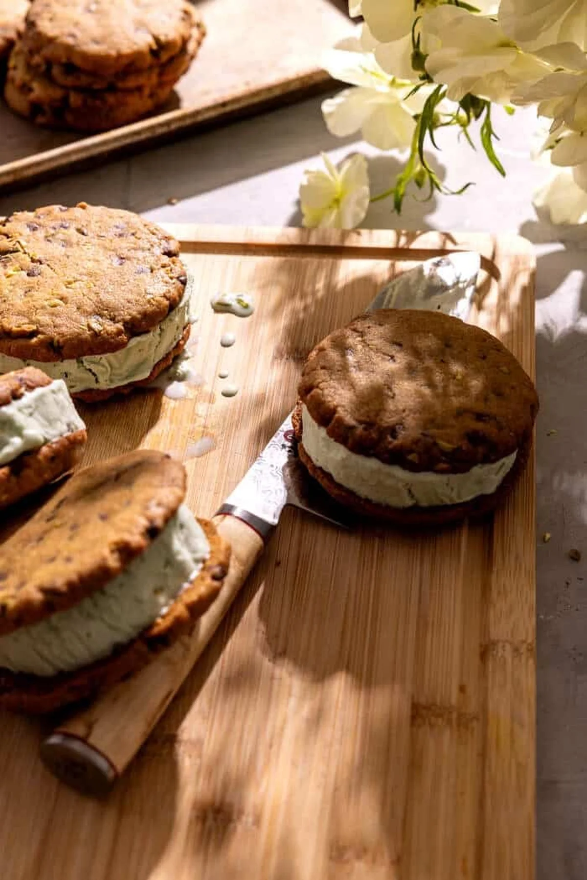 Assembled pistachio cookie ice cream sandwiches on a wooden board