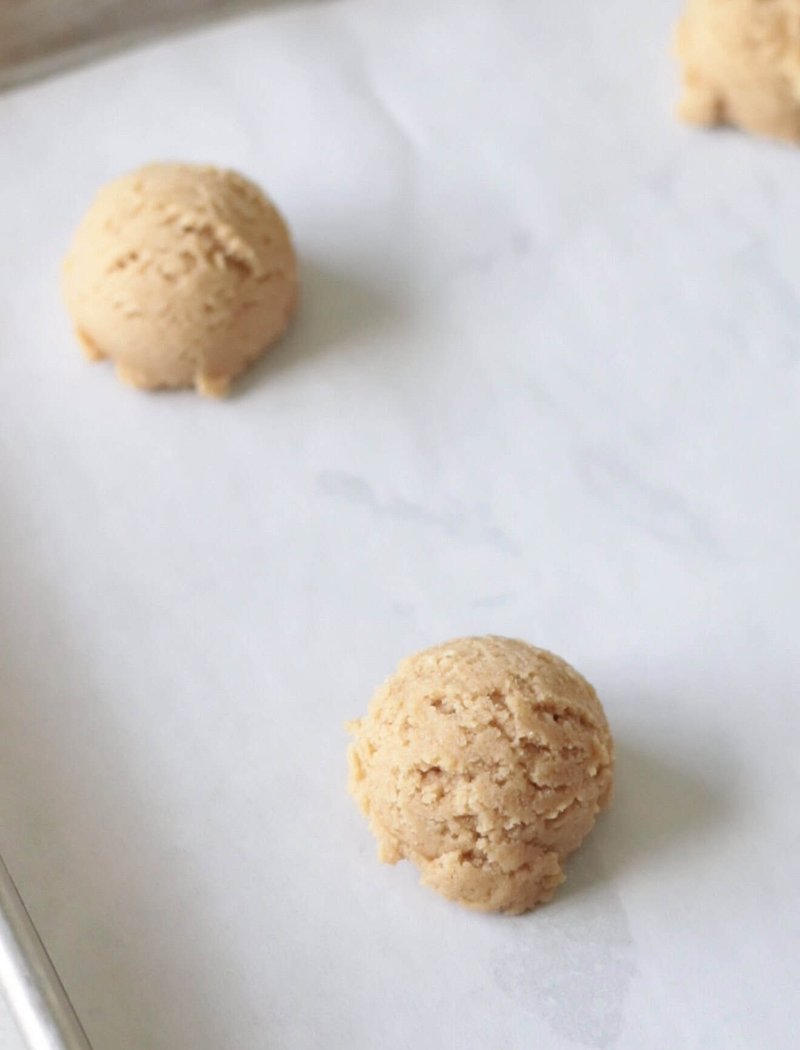 Scoops of raw cookie dough on a parchment-lined baking sheet