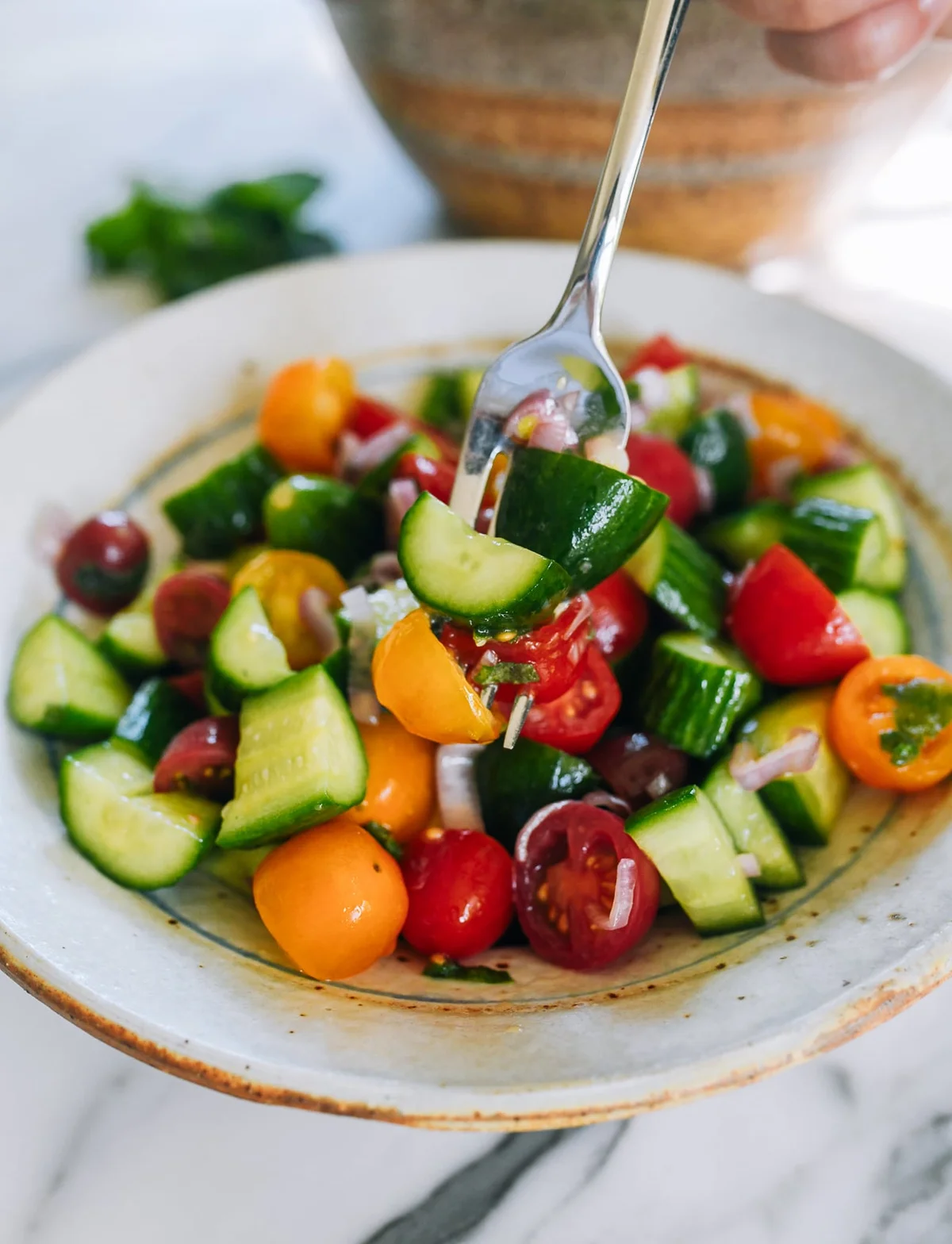 Cucumber tomato salad with mint in a bowl, fork lifting a portion