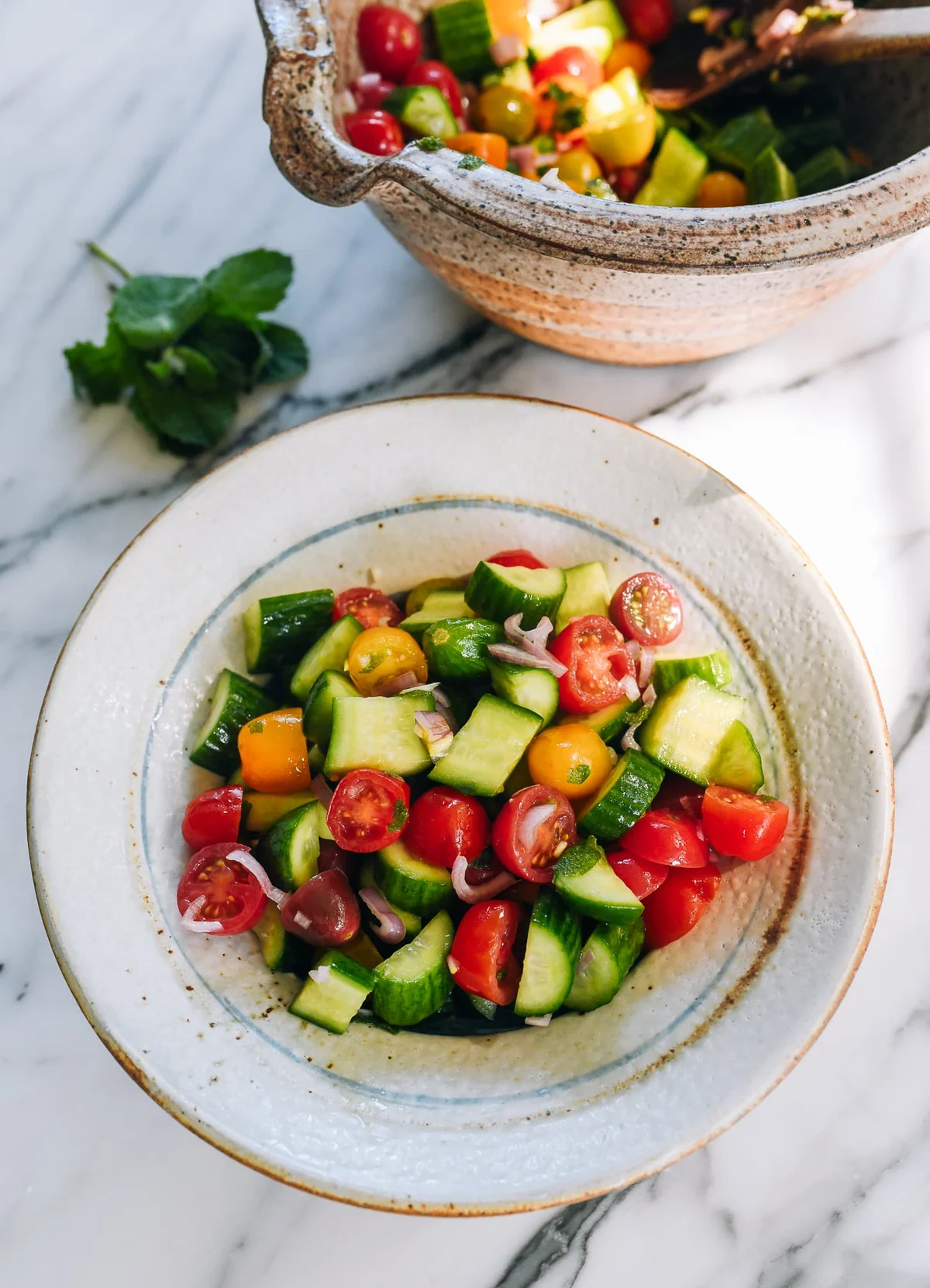 Finished cucumber tomato salad in ceramic bowl on marble