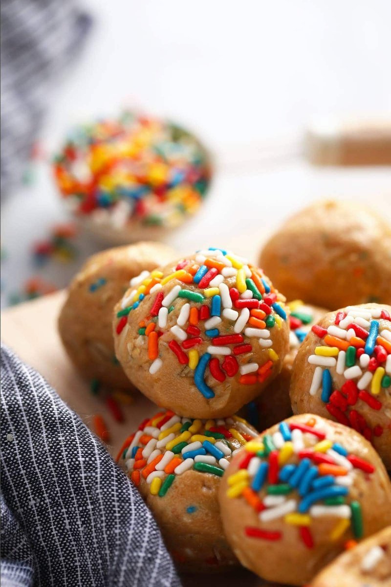 Rolled protein balls dusted in sprinkles stacked on a wooden surface