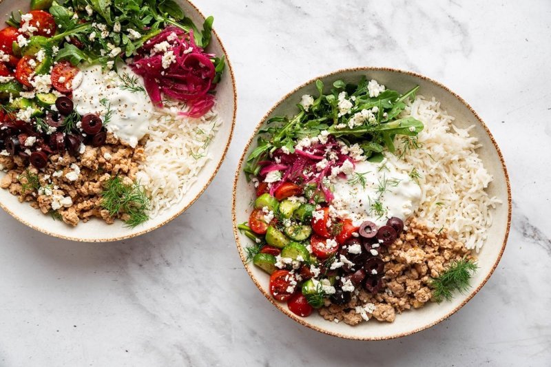 Two assembled Greek turkey bowls with rice, feta and vegetables